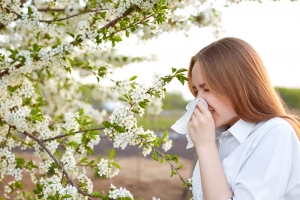 A woman suffering from allergy is standing near a blooming tree