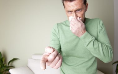 A man is sneezing because he is allergic to dust