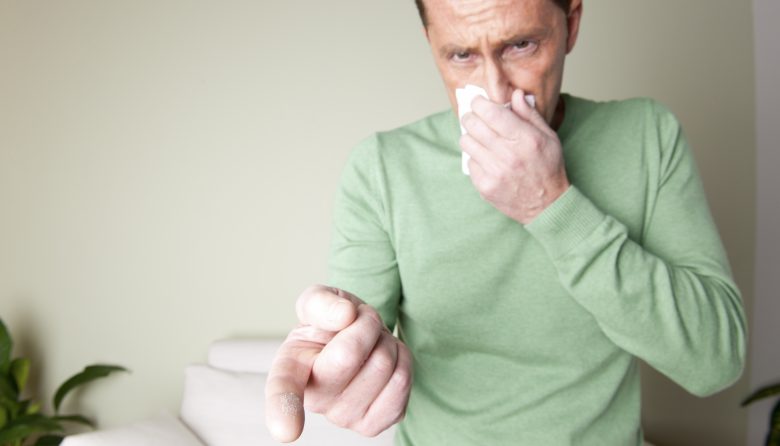 A man is sneezing because he is allergic to dust